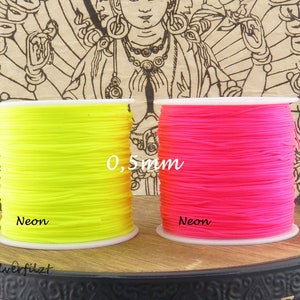 Könnte beinhalten: Zwei Spulen mit neonfarbenem Garn, eine gelbe und eine rosa. Die Spulen sind mit "Neon" beschriftet und das Garn ist 0,5 mm dick.