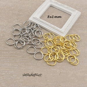 Könnte beinhalten: Eine Auswahl an silber- und goldfarbenen Sprungringen, mit einem weißen Rahmen im Hintergrund. Der Rahmen trägt den Text "8 x 1 mm". Das Bild enthält auch den Text "vollverfilzt".