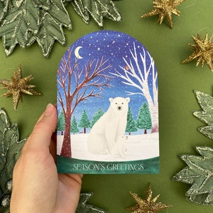 Season’s greetings snowglobe card with polar and baby cub in a woodland with a robin and squirrel in the background. Starry with a crescent moon and snow.
