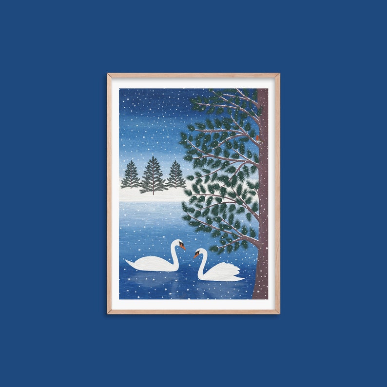 Christmas art print with mock up oak frame with 2 swans in a lake, a tree in the foreground with a robin perched on a branch and 3 christmas trees in the background. The daytime blue sky background and falling snow.