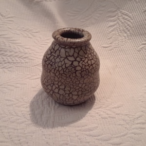 May include: A small, white ceramic vase with a crackled glaze. The vase has a rounded body and a slightly flared opening.
