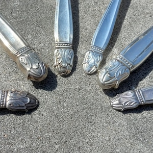 Puede incluir: Cinco cubiertos de servicio plateados con mangos ornamentados. Los mangos están decorados con un diseño floral.