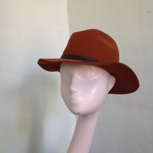 May include: A brown felt fedora hat with a brown leather band. The hat is on a white mannequin head.