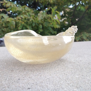 May include: A small, clear glass bowl with a gold iridescent finish. The bowl has a unique, organic shape and a small, curled handle.