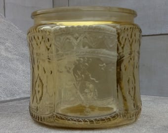 Pode incluir: Um frasco de vidro âmbar vintage com um padrão decorativo em relevo. O frasco tem uma boca larga e um fundo arredondado.