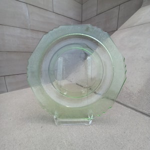 May include: A green glass plate with a scalloped edge and a floral design. The plate is on a white stand.