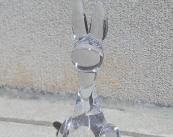 May include: A clear glass rabbit figurine with a round body and long ears. The rabbit is sitting on a gray surface.