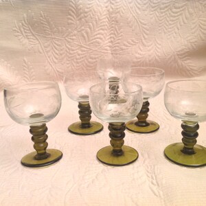 以下が含まれることがあります： エッチングされたデザインが施された、透明なガラス製の脚付きグラス6個セット。グラスは緑色のベースです。