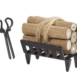 Könnte beinhalten: Ein Miniatur-Kamin-Set. Es besteht aus einem schwarzen Metall-Holzhalter, der mit Holzscheiten gefüllt und mit Bindfaden verschnürt ist. Eine Zange aus schwarzem Metall befindet sich links von den Holzscheiten.