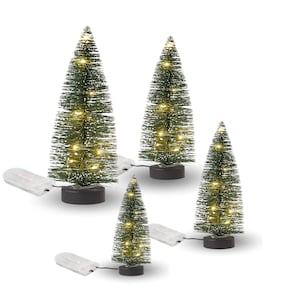 Könnte beinhalten: Vier kleine, grüne Weihnachtsbäume mit weißen Akzenten und warmweißen LED-Lichtern. Jeder Baum steht auf einem schwarzen Sockel und ist mit einem Batteriepack verbunden. Die Bäume sind vor einem weißen Hintergrund angeordnet.