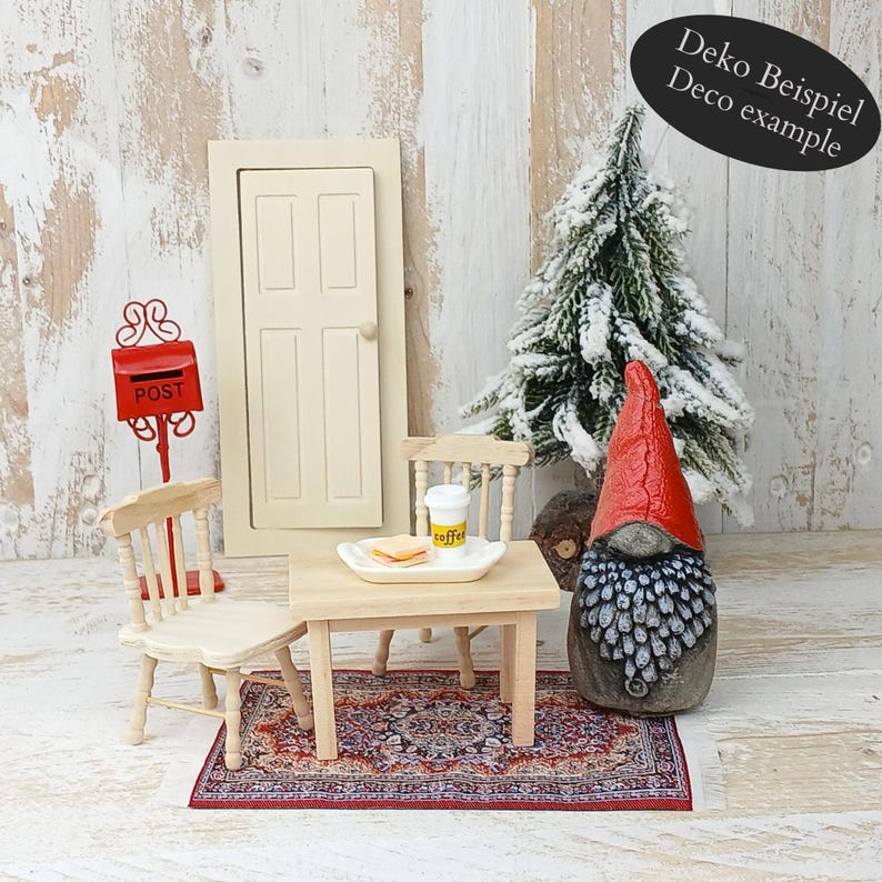 May include: Miniature scene with a red mailbox, a cream-colored door, and a small table set for a meal. A gnome with a red hat and a snowy Christmas tree add to the whimsical decor. The text "Deko Beispiel Deco example" is visible.