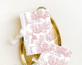 May include: Two white books with pink floral patterns and the words "Her Vows" and "His Vows" on the covers. The books are tied with white ribbon and are sitting on a gold tray.