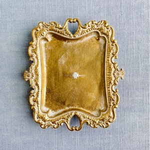 May include: A gold-toned ornate ring dish with a diamond ring in the center.