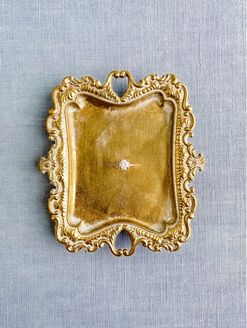 May include: A gold-toned ornate ring dish with a diamond ring in the center.
