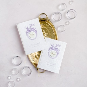 Op de afbeelding: Twee witte uitnodigingen met paarse bloemenmotieven en gouden waszegels op een gouden dienblad. De uitnodigingen zeggen "Mr. & Mrs." en hebben een datum.