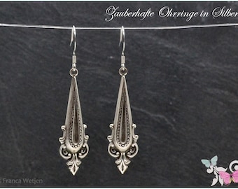 May include: A pair of silver dangle earrings with a teardrop shape and intricate details. The earrings are hanging from a white string.