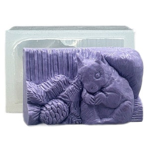 May include: Purple soap bar with a detailed design of a squirrel sitting next to a pine cone.