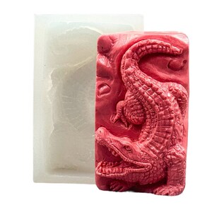 Puede incluir: Un molde de silicona rosa para hacer un jabón o una vela con forma de cocodrilo. El molde está detallado con escamas y una superficie texturizada.