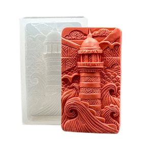 Puede incluir: Un molde de silicona rojo para hacer jabón o velas. El molde presenta un diseño detallado de un faro con olas rompiendo a su alrededor.