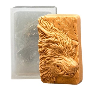 以下が含まれることがあります： 透明なシリコンモールドに入った、詳細で質感のある茶色のオオカミの頭部の彫刻。オオカミの顔は鋭い歯と眉間にしわを寄せ、うなり声をあげている。