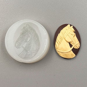 May include: A white, round mold and a gold-colored oval cameo featuring a horse head profile. The cameo is set against a dark brown background. The horse head is detailed with a bridle.