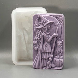 May include: A purple silicone mold for making soap. The mold features a witch with a cat and a broom, standing in front of a full moon.