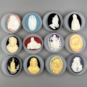 May include: Twelve round, white ceramic medallions with various religious figures and scenes. Each medallion is set in a silver-colored frame and features a different image, including a praying figure, a mother and child, and a saint.