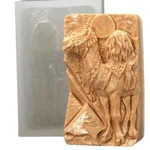 May include: A beige silicone mold with a detailed camel design. The camel is standing on a pyramid with a sun behind it. The mold is perfect for making soap, candles, or other crafts.