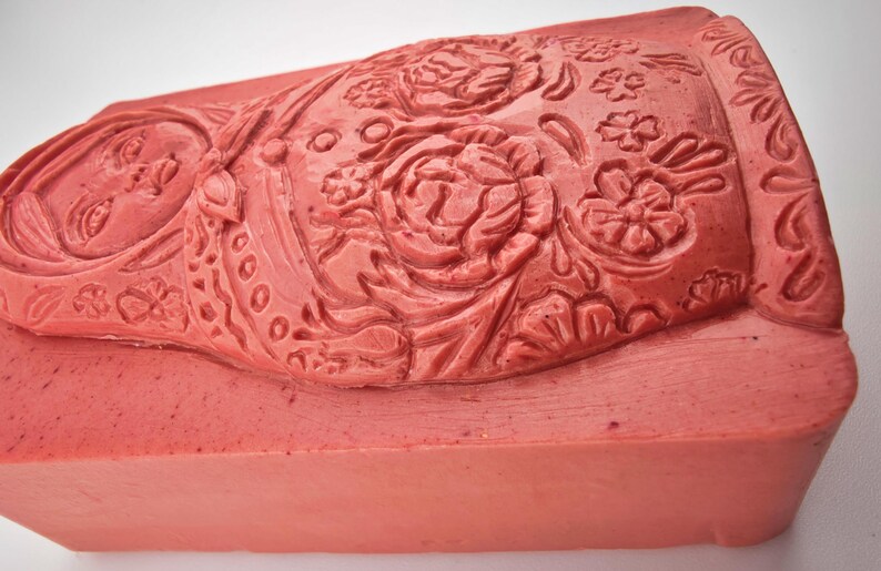 May include: A rectangular, coral-colored stamp with intricate floral and figure carvings. The design features a woman's face, roses, and other floral elements. The stamp is likely used for decorative purposes.