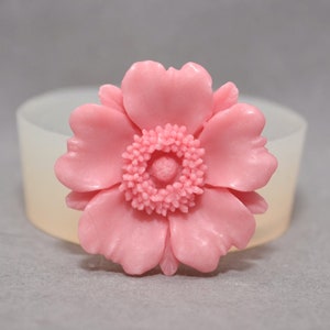 May include: A pink flower with five petals and a detailed center. The flower is made of a smooth, soft material and has a realistic appearance.