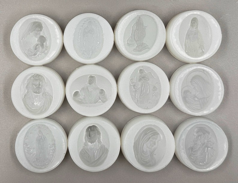 Puede incluir: Doce moldes redondos de silicona blanca con im&aacute;genes en relieve de figuras religiosas. Los moldes est&aacute;n dispuestos en cuatro filas de tres.
