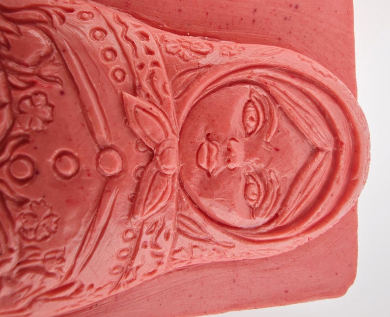 May include: A close-up of a red-toned carving of a Matryoshka doll. The doll's face and floral details are intricately carved. The carving is on a rectangular base.