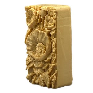 May include: A rectangular bar of soap with a detailed floral design. The soap is beige and features a raised design of poppies and leaves.