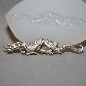 以下が含まれることがあります： 鱗模様が細かく表現された銀色のドラゴン像。腹ばいになって横を向いている。