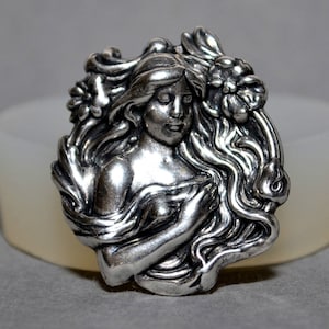 May include: A silver-toned pendant featuring a detailed sculpted design of a woman with flowing hair and floral accents.