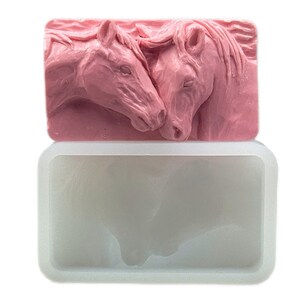 K&ouml;nnte beinhalten: Eine rosa Silikonform zum Herstellen von Seife oder Kerzen. Die Form zeigt ein detailliertes Design von zwei Pferdek&ouml;pfen, die sich die Nasen ber&uuml;hren.