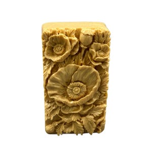 May include: A rectangular bar of soap with a detailed floral design. The soap is a light beige color and features a raised design of poppies and leaves.