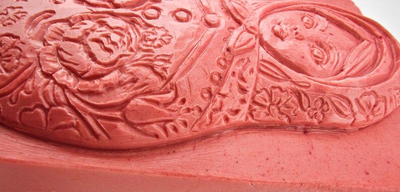 May include: Close-up of a red rubber stamp with a detailed relief design. The stamp features floral and human figure motifs, with intricate patterns and textures. The design is carved into the red rubber surface.