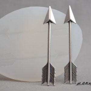 Puede incluir: Un par de pendientes de flecha de plata con un diseño sencillo. Las flechas son puntiagudas y tienen una cola de plumas.