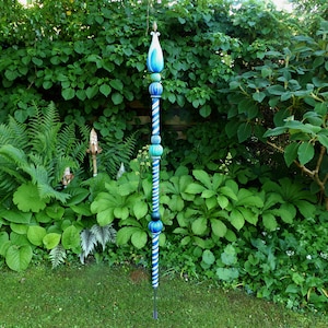 Op de afbeelding: Een hoge, decoratieve tuinpaal met een blauw-wit gestreept ontwerp. De paal heeft een puntige top en is versierd met blauwe en zwarte kralen.