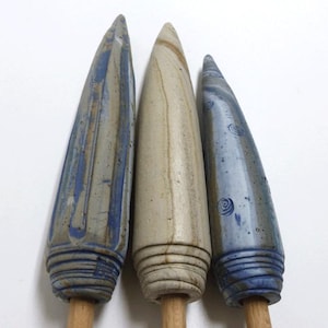 Op de afbeelding: Drie keramische flesstoppers met houten handvatten. De stoppers zijn kegelvormig, met blauw en bruin glazuur. De stoppers hebben een textuur en zijn van verschillende afmetingen. De stoppers worden gepresenteerd tegen een witte achtergrond.