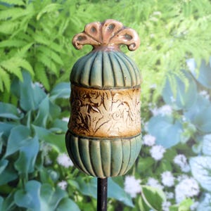 Op de afbeelding: Een keramische tuinpaal met een tealgroen en bruin bloemenontwerp. De bovenkant van de paal is een decoratief eindstuk met een roze en witte glazuur.