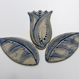 Peut inclure: Trois carreaux en céramique en forme de fleur avec un glaçage bleu et blanc. Le carreau central est en forme de tulipe et les deux carreaux extérieurs sont en forme de feuilles.