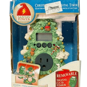 May include: A Christmas tree-shaped digital timer with a removable LCD timer. The green tree has white accents, decorative ornaments, and a power outlet. The packaging includes the text "SANTA'S POWER" and "DIGITAL TIMER".