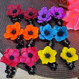 Puede incluir: Surtido de pendientes de colores en forma de flor con detalles de cuentas negras. Los pendientes están hechos de arcilla polimérica y presentan una variedad de colores, incluyendo rojo, azul, amarillo, verde y morado.