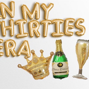 May include: Gold foil balloons spelling "In My Thirties Era" with a gold crown, a green bottle of champagne, and a gold champagne flute.