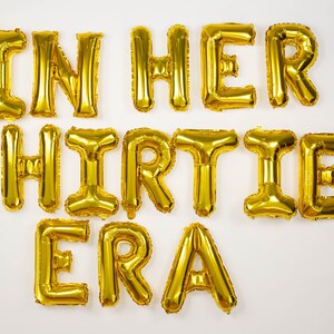 May include: Gold foil letter balloons spelling out "In Her Thirties Era".