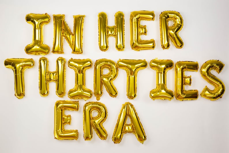 May include: Gold foil letter balloons spelling out "In Her Thirties Era".
