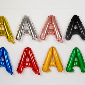May include: A set of eight letter A balloons in different colors, including gold, silver, rose gold, black, blue, red, yellow, and green.