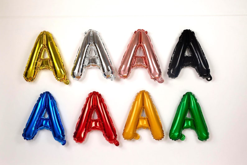 May include: Eight foil balloons shaped like the letter "A" in various colors: gold, silver, rose gold, black, blue, red, yellow, and green. The balloons are arranged against a white background.